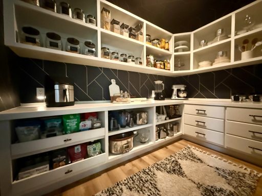 Modern kitchen with white cabinets, dark backsplash, and organized storage containers.
