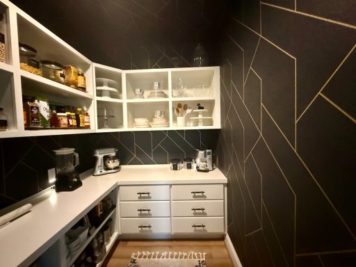 Contemporary pantry with dark walls, white shelves, and organized kitchen supplies.