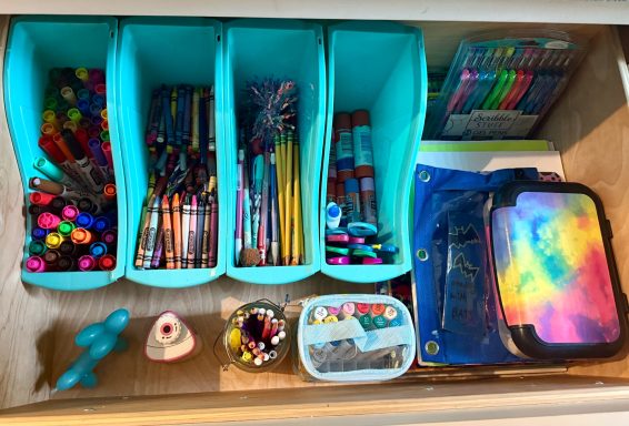 Organized drawer with colorful pens, pencils, markers, and stationery items in containers.
